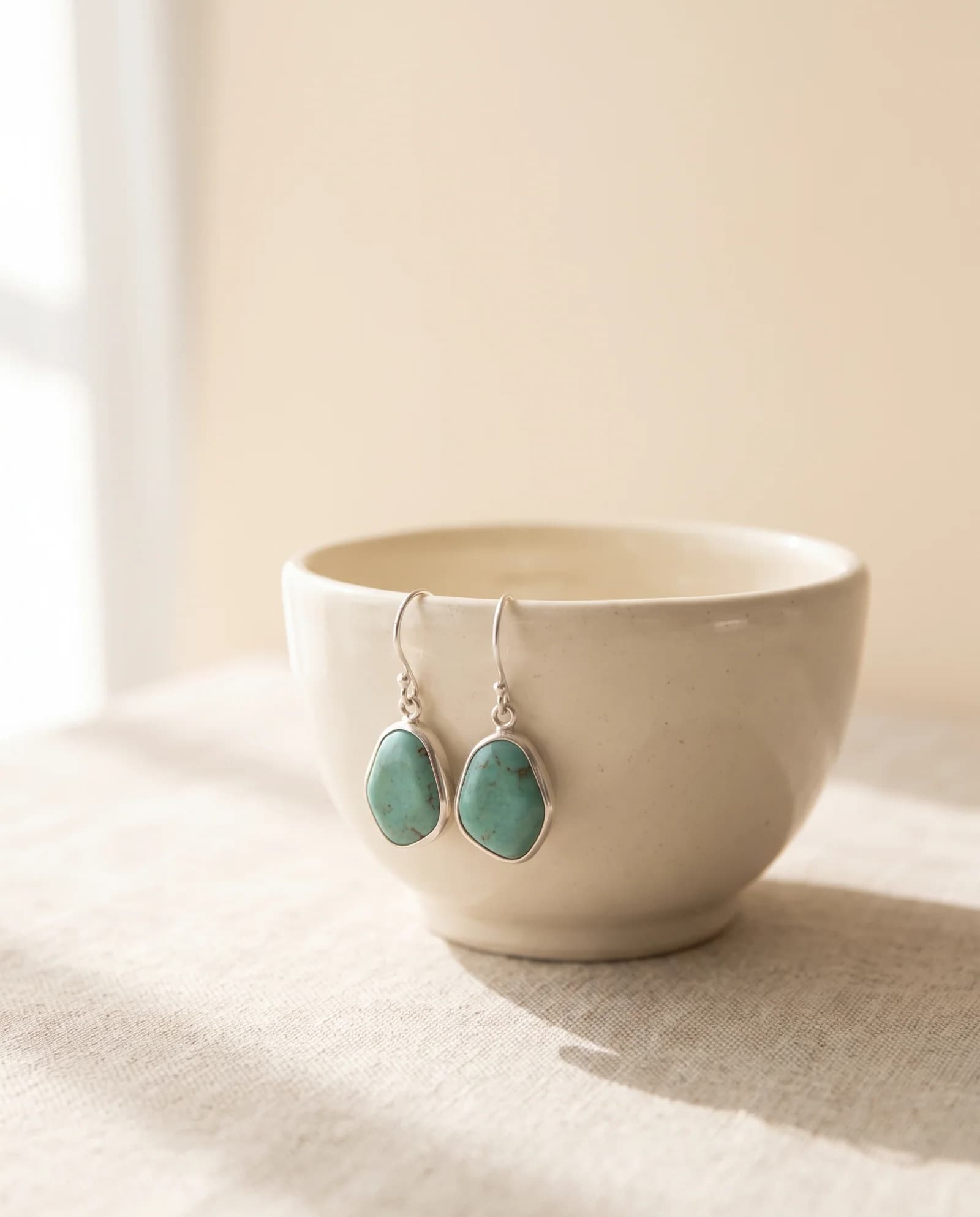 Silver drop earrings with turquoise stones hanging from a ceramic bowl