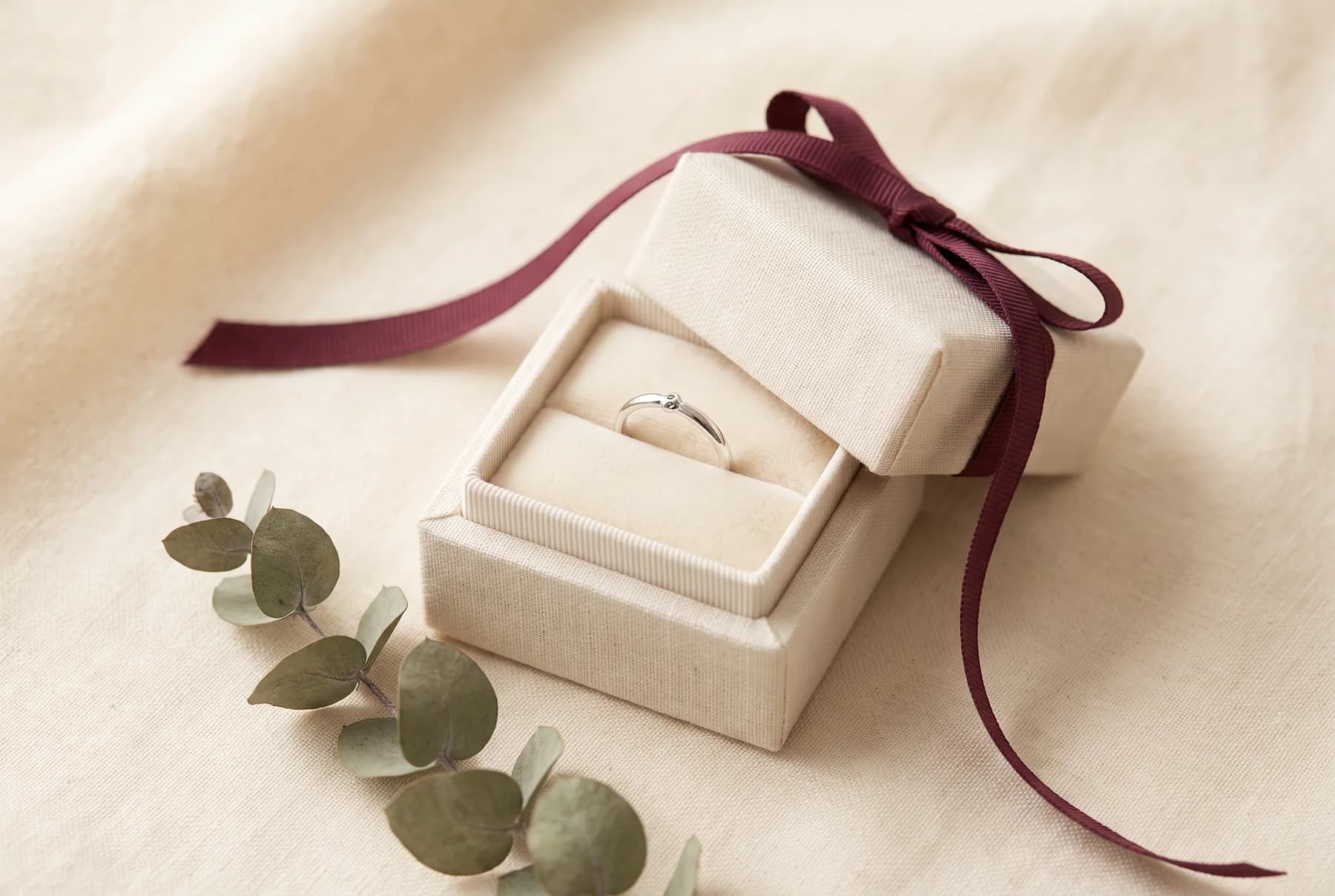 Cream linen gift box tied with a wine ribbon holding a silver ring